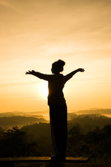 silhouette of free cheering woman open arms at mountain peak sunrise