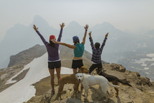 Rear View Of Friends With Arms Raised Standing By Dogs On Mountain
