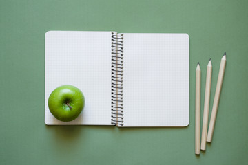 Wall Mural - Clean open notebook with space for the text, pencils and apple on a green surface. Top view