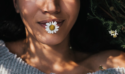 Cropped close-up horizontal shot of brunette young girl with daisy flower in mouth outdoors enjoying nature. Portrait of an attractive Caucasian woman feel free with copy space. Cover idea mood