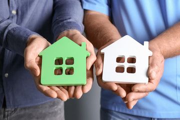 Canvas Print - Real estate agent and senior man holding house models, closeup