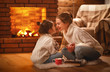 © JenkoAtaman - family mother and child drinking tea and laughing on winter evening by fireplace.