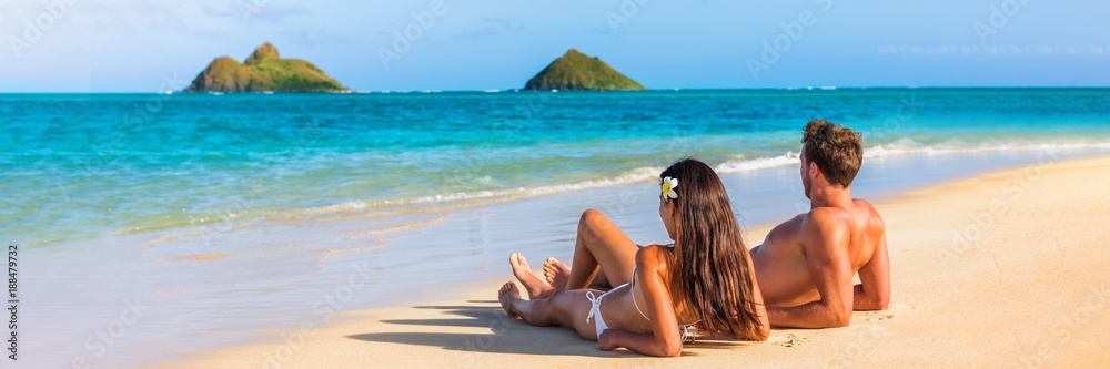 Hawaii travel summer vacation couple on hawaiian tropical beach in Lanikai, Oahu, Hawaii, US. American tourists people on holidays lying down, panoramic banner crop with moke islands in background. - obrazy, fototapety, plakaty 