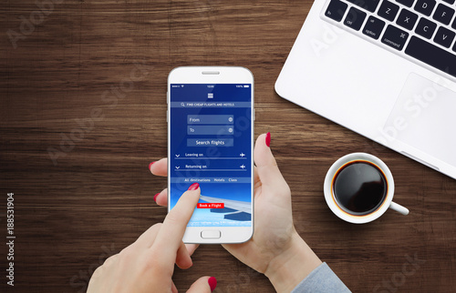Fotografía Female person using cheap flights app on her smartphone while sitting at the des