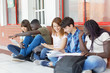 © jovannig - Multi ethnic teenagers friends making school tests outdoor, seated in the school courtyard