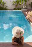 Fototapeta  - back view of young woman in swimsuit and hat sitting in pool of hotel