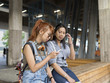 © Scandinav - Two girl sitting on bench looking at smartphone