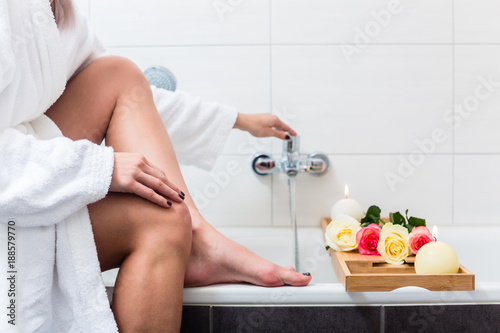 Fotografie, Obraz Woman preparing wellness bath with flowers, candles and fragrance oil in tub