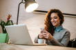 © bnenin - Smiling beautiful white caucasian girl with curly hair sitting at desk and using phone.