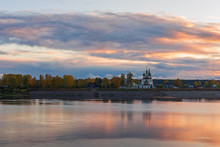 View Of A Russian Village With A Church On The River Bank At Sunset