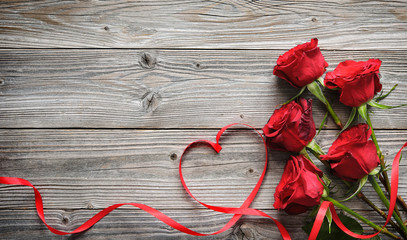 Romantic floral frame with red roses and ribbon on wooden background