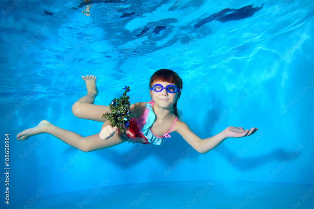 Underwater in swimming pool little girl swims with a toy in hand ...
