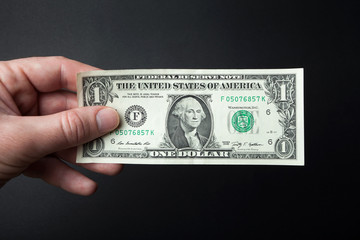 Hand and one dollar bill on a black background.