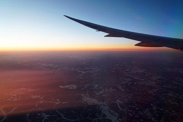 Wall Mural - red sunlight spreading on aerial cloud and land below airplane wing