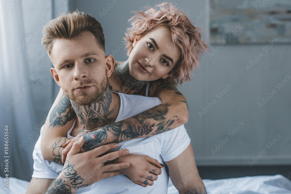 smiling tattooed girl hugging her boyfriend on bed in bedroom Stock ...