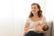 Cheerful young woman breastfeeding infant child at home. 