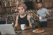 © LIGHTFIELD STUDIOS - tattooed girl using laptop during breakfast, boyfriend behind in kitchen