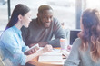 © zinkevych - International friendship. Positive colleagues sitting around wooden table and looking at their notes while discussing some points