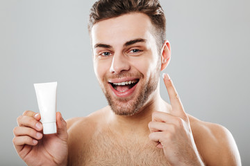 Wall Mural - Beauty and skincare of happy shirtless man applying face cream in morning isolated over gray background