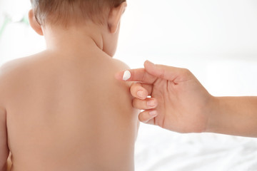 Woman applying body cream on her baby against light background