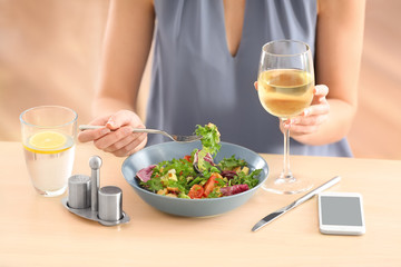 Wall Mural - Young woman drinking wine and eating salad at table