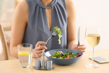 Wall Mural - Young woman eating fresh salad at table