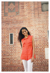 Wall Mural - Portrait of attractive, young Indian woman standing in front of a brick wall in a city. She's laughing and is stylish. 