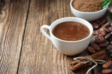 cocoa drink in white mug, cocoa powder and cocoa beans on wooden table.