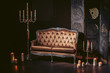 A luxurious sofa made of golden fabric in a modern interior decorated with decor and candles. In dark colors.