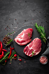 Canvas Print - Raw pork meat. Fresh steaks on slate board on black background. Top view