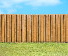 Generic Wooden Residential Privacy Fence With  A Lush Green Grass Yard In The Foreground And A Beautiful Blue Sky With Fluffy Clouds.