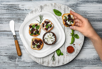 Poster - Woman holding tasty bruschetta with sun-dried tomatoes over wooden board, top view