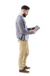 © sharplaninac - Stylish hipster businessman holding and watching tablet pad computer. Side view. Full body length portrait isolated on white studio background.