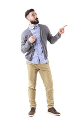 Wall Mural - Uncertain confused bearded man pointing fingers up and looking above. Full body length portrait isolated on white studio background. 