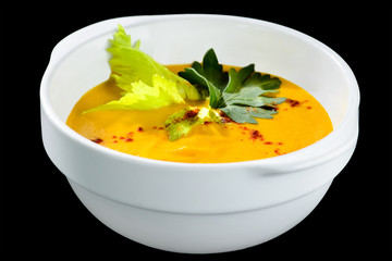 Wall Mural - Healthy tasty carrot cream soup with parsley in a white plate isolated on black background