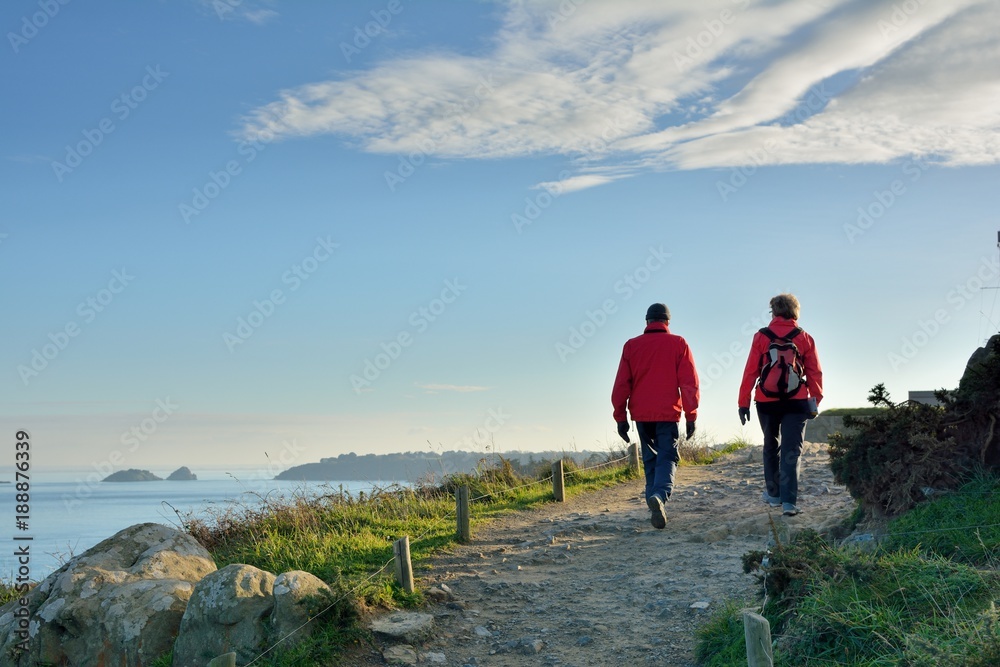 Un couple de randonneurs qui marche sur le sentier côtier à la pointe du Grouin à Cancale en Bretagne - obrazy, fototapety, plakaty 