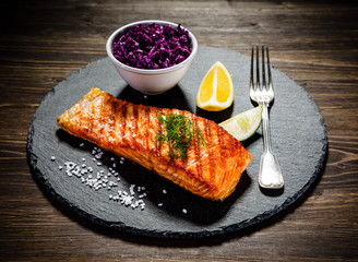 Grilled salmon with vegetables served on black stone plate on wooden table