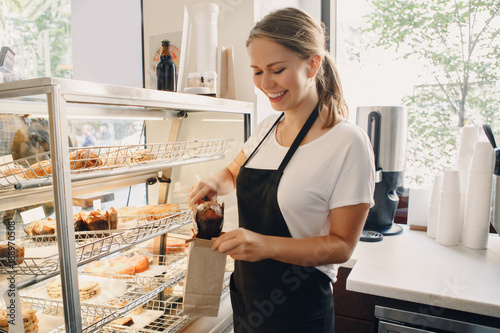 Fotografía Portrait of white Caucasian beautiful barista woman taking muffin pastry from shop-window