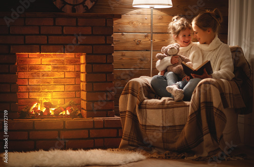 Photographie happy family mother and child daughter read book on winter evening near fireplac