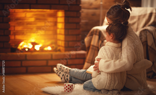 Fotografía family mother and child hugs and warm on winter evening by fireplace