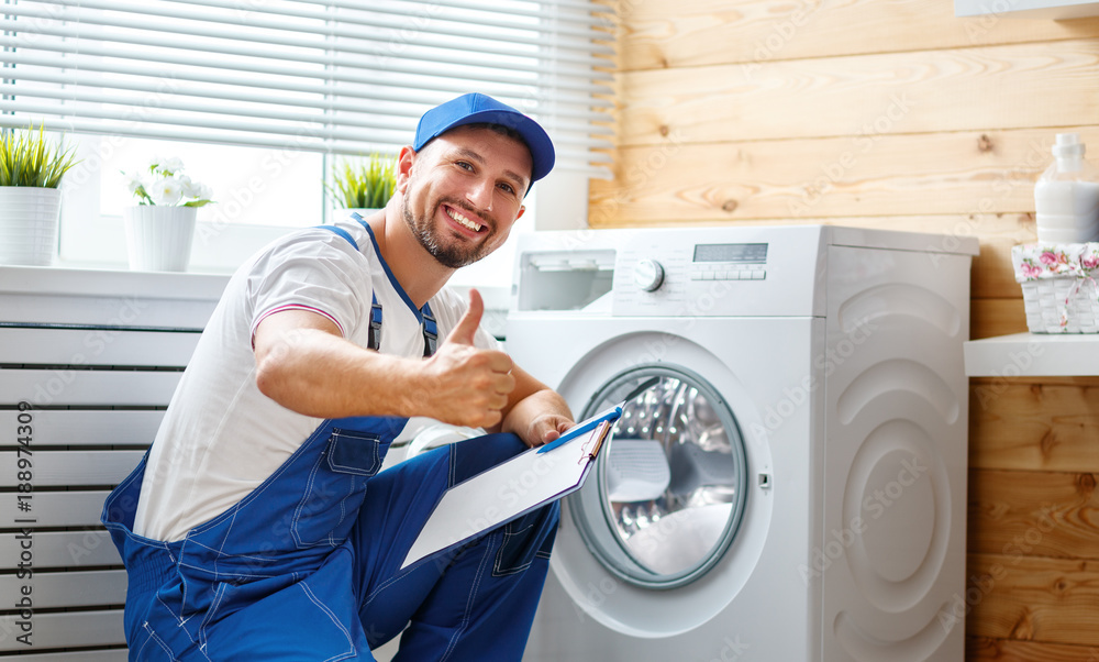 working man   plumber repairs  washing machine in   laundry - obrazy, fototapety, plakaty 