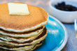 Stack of pancakes with butter on a blue plate and blueberries in the background