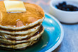 Stack of pancakes with butter and syrup on a blue plate and blueberries in the background