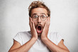 © WHstudio Leushin N - Scared frightened male looks with terror at camera, being afraid of something scaring, watches horror film, poses against white concrete wall. Fashionable stylish male nerd demostrates his phobia