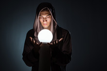 Young Wizard With Crystal Ball In Dark Room