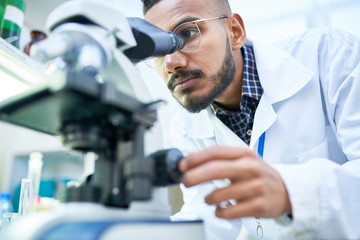 portrait of young middle-eastern scientist looking in microscope while working on medical research i