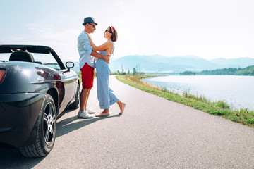 Wall Mural - Couple in love stands near the cabriolet car on the picturesque mountain road