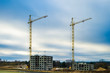 Tower cranes and unfinished multi-storey high near buildings under construction site in cloudy day in the evening with dramatic colorful cloud background