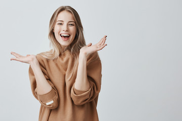 Wall Mural - Pretty beautiful woman with blonde long hair looking at camera having excited and happy facial expression, clapping with her hands against blank studio wall, expressing her excitement with present