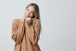 Beautiful blonde woman expresses happy emotions, in brown sweater, has broad pleasant smile, glad to recieve present. Smiling overjoyed female model enjoys life, isolated against gray background